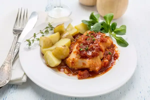 Un succulento merluzzo bollito in salsa di pomodoro, accompagnato da patate novelle e un rametto di timo.