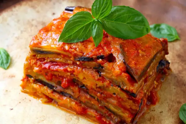 Una fetta di parmigiana di melanzane ricetta originale, stratificata e succulenta, guarnita con basilico fresco.