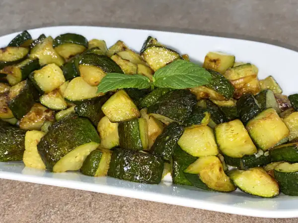 Un piatto di zucchine trifolate, tagliate a cubetti e cotte fino a doratura, guarnite con una fogliolina di menta.