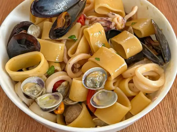 Un piatto invitante di calamarata allo scoglio, con pasta grossa, cozze, vongole e anelli di calamaro, condito con pomodorini e prezzemolo.