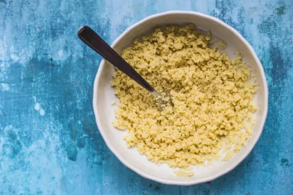 Ciotola di cous cous pronto per essere condito, con una forchetta che affonda nei granelli dorati.