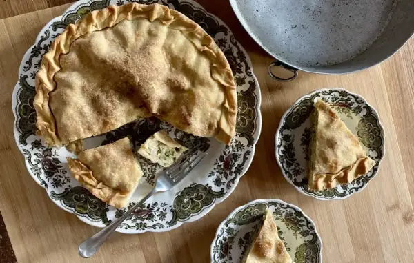 Una torta di riso e zucchine alla ligure, dorata e invitante, servita su un piatto decorato. Due fette sono già state tagliate, pronte per essere gustate.