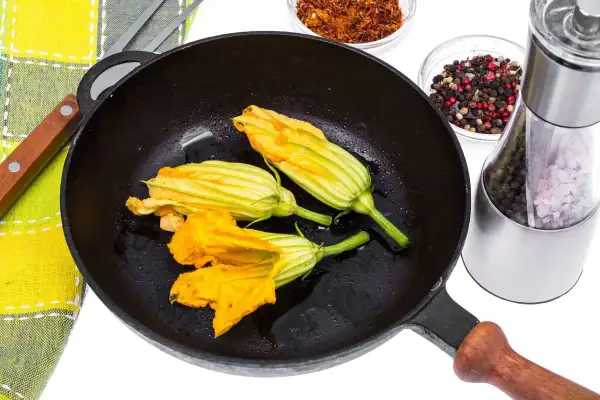 Fiori di zucca in padella, pronti per essere impanati e fritti. Accanto, spezie e un macina sale.