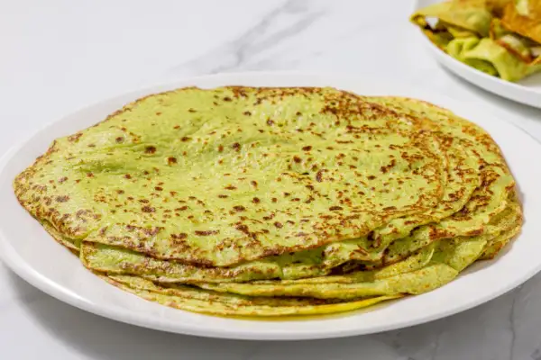 Piatto di crepes di zucchine verdi, sottili e leggermente dorate, impilate su un piatto bianco.