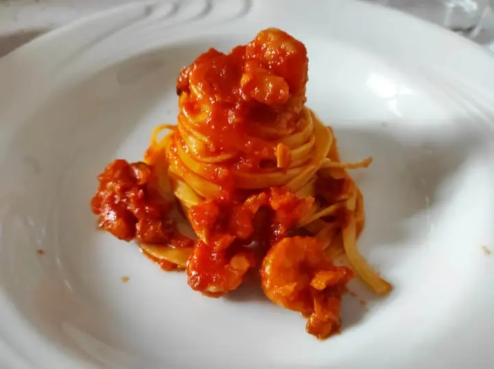 Un nido di pasta fresca avvolto in un ricco sugo di pesce, con gamberi succulenti che si adagiano sul piatto bianco.